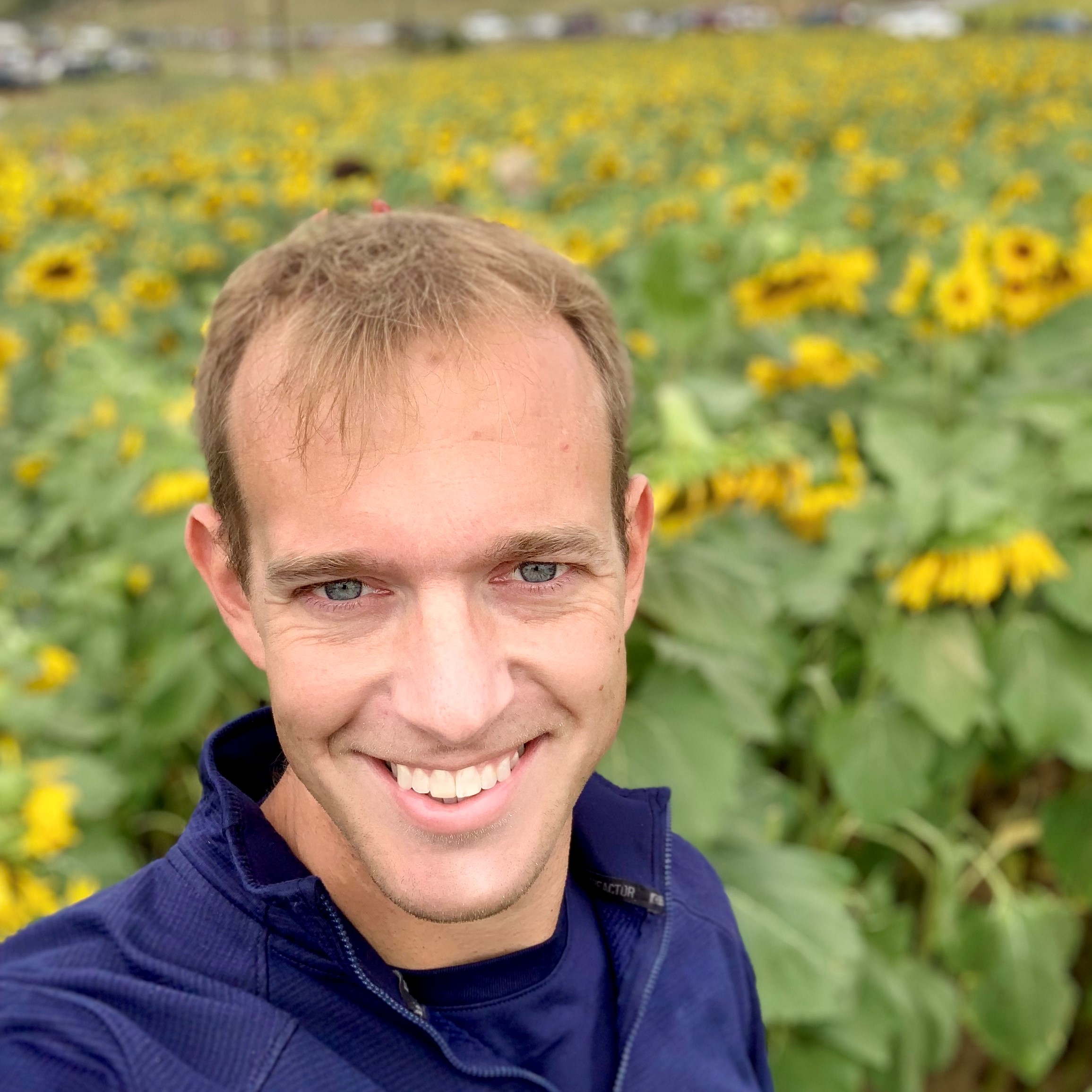 Me, smiling happily at the camera with a field of sunflowers in the background.